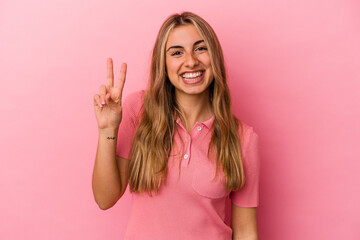 Fototapeta na wymiar Young blonde caucasian woman isolated on pink background showing victory sign and smiling broadly.
