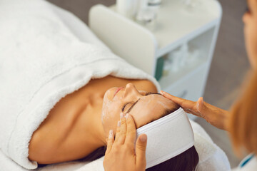 Hands of cosmetologist making facial massage with cream for woman in beauty salon