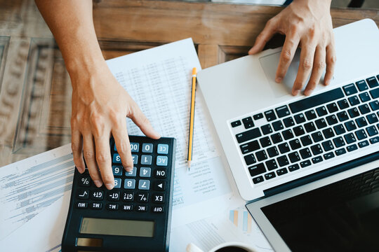 businessman hand using calculator for calculate about cost, tax or budget and cheking with data in laptop on the table in office.