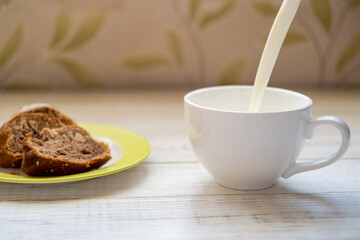 Milk is poured into a cup. Morning breakfast with a muffin.