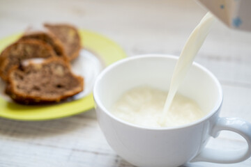 Milk is poured into a cup. Morning breakfast with a muffin.