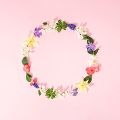 A circle of flowers, leaves and branches on pink background with copy space.