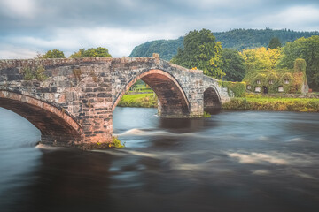 Old Roman inspired bridge Pont Fawr across the River Conwy towards a 15th century ivy covered stone...