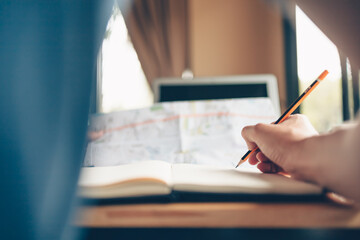 Tourist planning vacation in earphone use pencil short note in book and travel accessories around on the table. Vocation, travel, holidays and backpack concept.