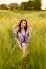 Stylish girl in violet dress and hat in field. Happy young woman on the sunset or sunrise in summer nature. Fashion and lifestyle concept.