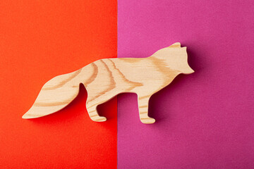 A figurine of a fox with a fluffy tail, carved from solid pine with a hand jigsaw. On a multi-colored background