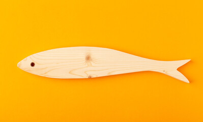 A figurine of horse mackerel, carved from solid pine by hand jigsaw. On a yellow background