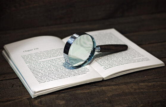 Image of a book and a magnifying glass, on a wooden background