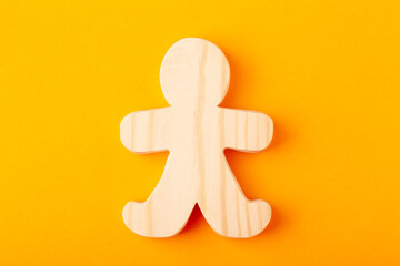 A figurine of a toy man carved from solid pine with a hand jigsaw. On a yellow background