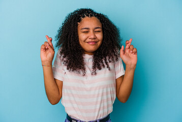 Young african american woman isolated on blue background crossing fingers for having luck