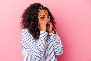 Young african american woman isolated on pink background blink through fingers frightened and nervous.