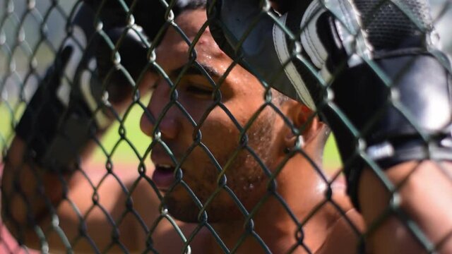 Hombre moreno con guantes de boxeo cansado apoyado en una reja pensativo