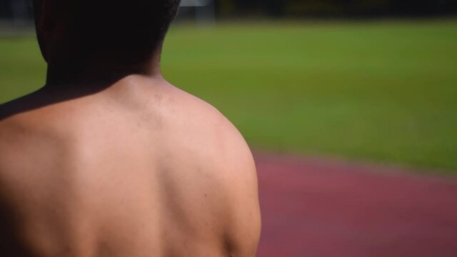 Hombre moreno de espaldas quit&aacute;ndose un buso rojo en una cancha de atletismo