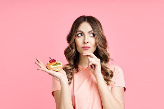 Dieting concept, confused pretty woman looking up holding pastry cake in hand