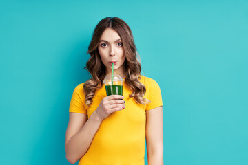 Pretty woman drinking tasty green detox juice on blue background