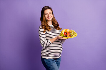 Photo of adorable sweet woman expecting child wear striped shirt belly holding fruit plate isolated purple color background