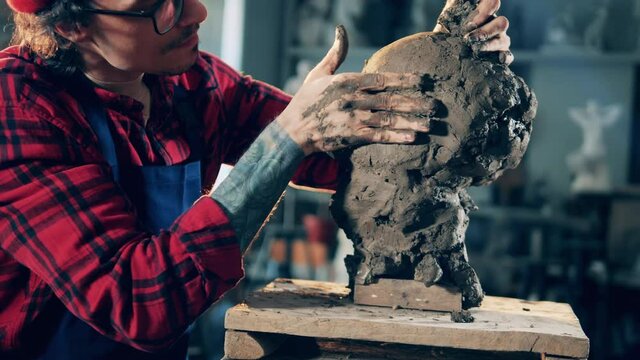Clay sculpture is getting kneaded by a male artist. Art concept, artist work in design studio.