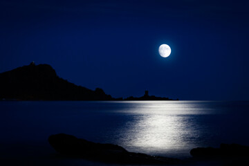 Super Moon over sea horizon with silhouette of rocky cape