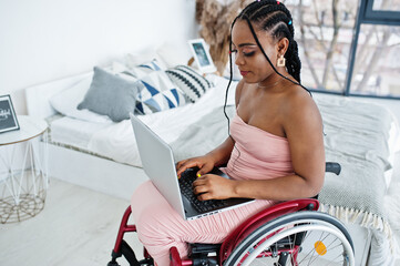 Young disabled African American woman in wheelchair at home working with laptop.