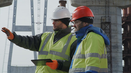 Male engineers discussing bridge drafts on tablet