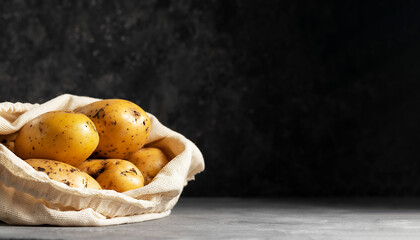 Raw early potato tubers in a beige eco friendly bag on a dark background copy space for text