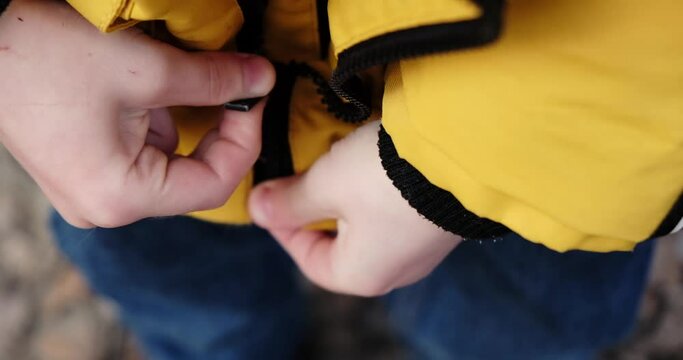 The child zips up the jacket. The boy's awkward movements.