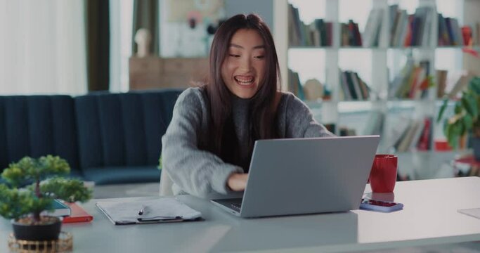 Young cheerful asian woman learning good news on internet, rejoicing and clenching her fists, celebrating salary day at home. Freelancer. Rich lifestyle.