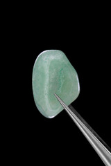 Green Aventurine jewel stone texture in tweezers on black background. Macro closeup.