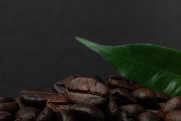 Roasted coffee beans with leaf on the old dark wooden background for wallpaper or decor. Shallow depth of field. Selected focuse