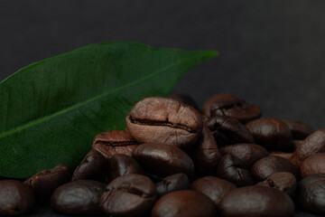 Roasted coffee beans with leaf on the old dark wooden background for wallpaper or decor. Shallow depth of field. Selected focuse