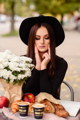 Young woman in hat drinking coffe at cafe terrace with white flowers.