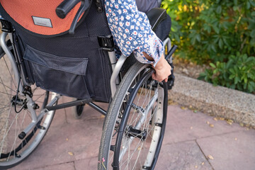Asian middle-aged lady woman patient sitting on wheelchair in park; healthy strong medical concept