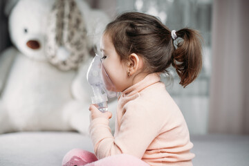 Fototapeta premium little cute girl sitting on the bed in the bedroom doing inhalation by herself