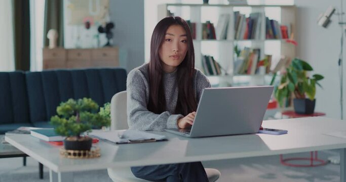 Asian young woman business freelancer working from home videochatting meeting conference on laptop and posing to camera inside home.