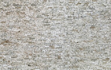 Large wall made of  small natural stone bricks. Color is  light gray with brown stains. Background and texture.