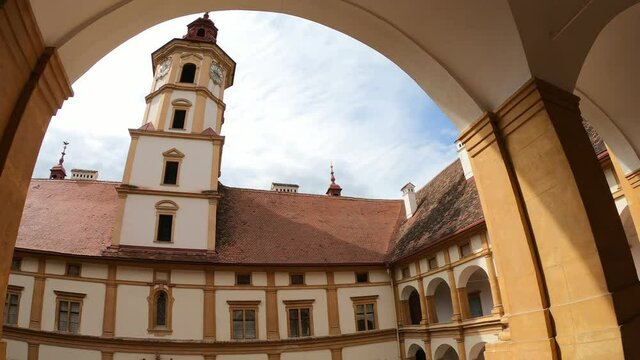A walk through the cloisters of Eggenberg castle in Graz, Austria. There is a square patio in the middle part with a tall bell tower. Clear and sunny day. Appreciation and contemplation of art
