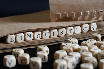 The word linguistics is made with wooden cubes next to a notebook made of eco-friendly paper. Concept of studying modern language sciences and teaching in school or college - obrazy, fototapety, plakaty