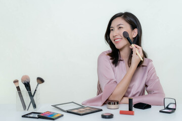 An Asian blogger beauty blogger shooting a video of herself wearing an orange lipstick in a studio.