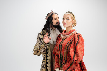 hispanic king in crown and medieval clothing looking at blonde wife isolated on white