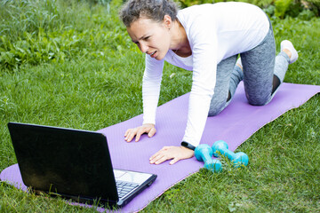 Tired exhausted young woman looking at laptop after personal trainer instructions via video online,...