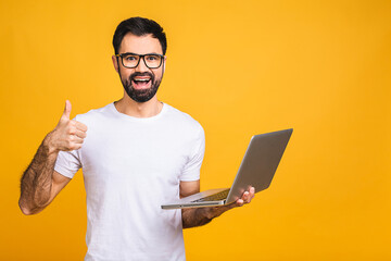 Confident business expert. Confident young handsome man in casual holding laptop and smiling while standing isolated over yellow background. Thumbs up.