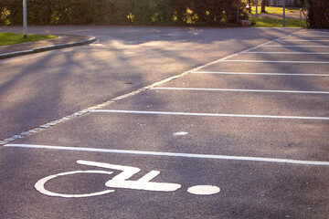 Empty parking lot, white lines on the asphalt, sunny day. Handicapped parking space at a parking lot outside a building, icon, sign painted on the designated parking space for disabled persons.