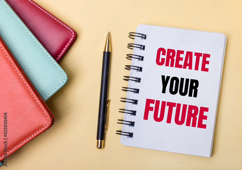 Aufkleber multi-colored diaries lie on a beige background next to a pen and a notebook with the words create y