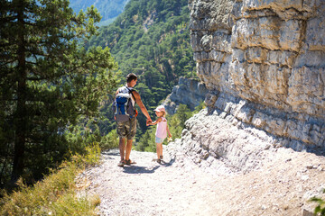 Dad and daughter go hiking on a mountain trail. Active family holidays, healthy lifestyle, trekking with a backpack, adventures of a young tourist.
