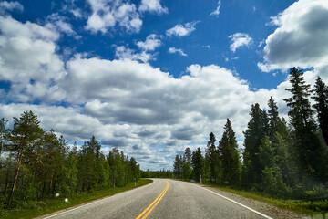 View from relief car windscreen on the blue sky with white clouds, grey asphalt road and landscape with forest and green teeses. Landscape through window
