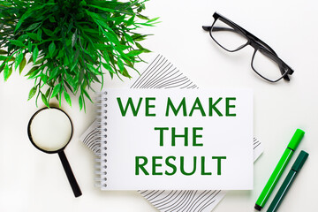 On a white background lies a notebook with words WE MAKE THE RESULTS, glasses, a magnifying glass, green markers and a green plant