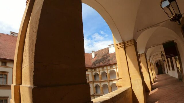 A walk through the cloisters of Eggenberg castle in Graz, Austria. There is a square patio in the middle part with a tall bell tower. Clear and sunny day. Appreciation and contemplation of art
