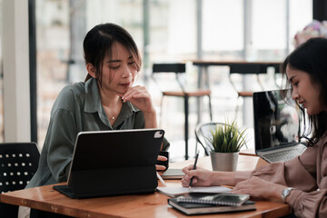 Young Asian businesswoman taking notes brainstorm collaboration using a tablet at the office.
