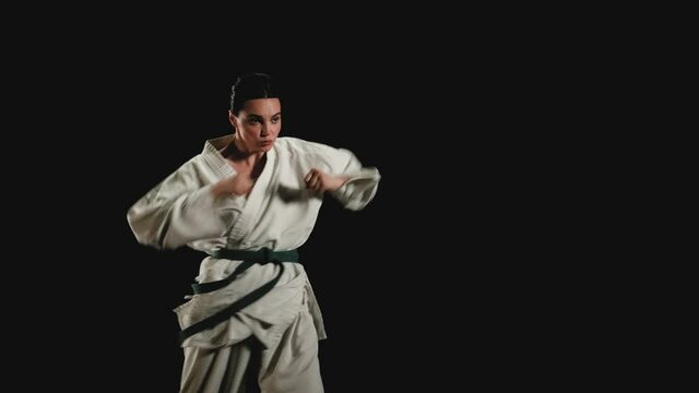 Woman in kimono practicing karate kicks on a black background