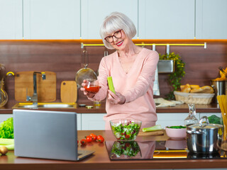 senior cheerful woman video blogger showing celery and tomato juice at her kitchen. Raw,...